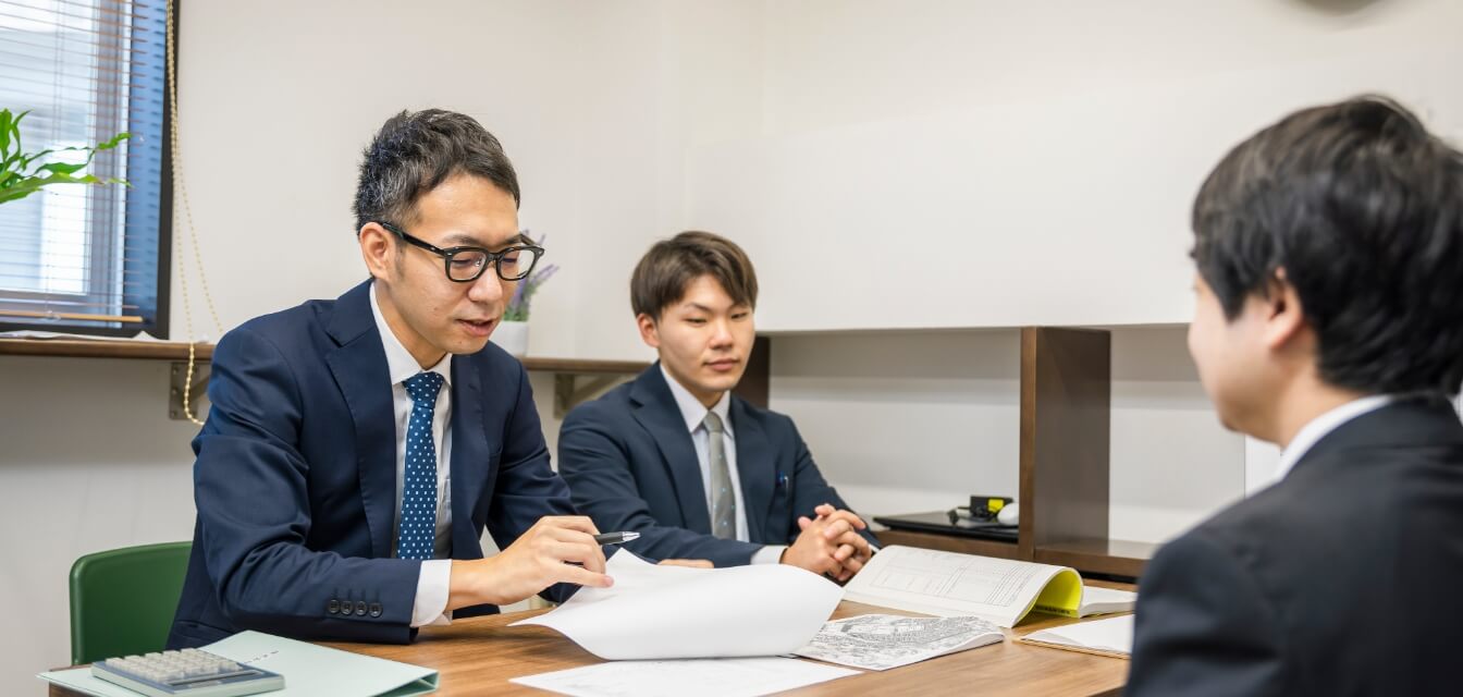 テーブルを囲んでお客さんと商談をする2名のスタッフ