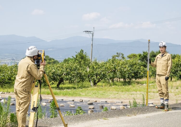 屋外で測量機器を操作する2名の作業員
