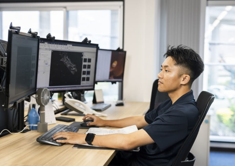 3Dモデルが表示されたモニターに向かって作業する男性スタッフ
